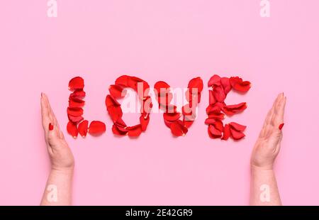 Flat Lay avec mot d'amour des lettres pétale roses rouges, sur fond rose. Les mains de femme enreplient le mot amour. Un concept romantique pour la Saint-Valentin. Banque D'Images