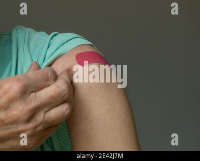 Homme caucasien senior tenant la manche de chemise pour montrer le bandaid après la vaccination du coronavirus dans l'épaule Banque D'Images