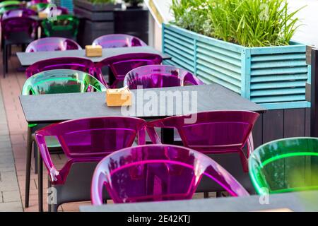 une table en bois avec un porte-serviette et des chaises en plastique multicolores sur la terrasse d'un café de rue avec des sièges gratuits, personne. Banque D'Images