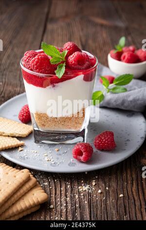 Pas de dessert au cheesecake dans un pot en verre recouvert de purée de framboises et baies fraîches sur fond de bois rustique Banque D'Images