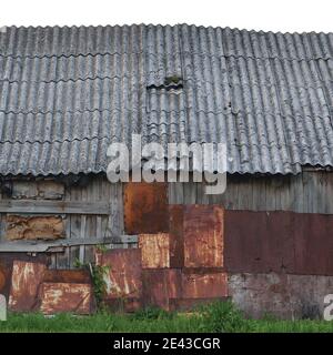 Ancienne cabane en bois vieillie, mur de cabane en bois plaqué gris, toit en ardoise, plaques de métal rouillées, texture de peinture rouillée, clôture isolée Banque D'Images