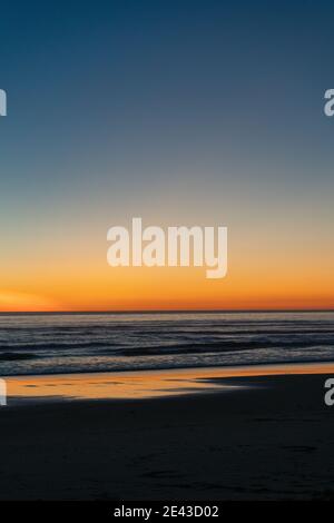 Reflet du coucher de soleil rouge sur le sable humide la plage et l'horizon sombre Banque D'Images