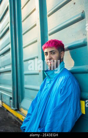 Homme tendance avec des cheveux teints roses stylés portant une veste rétro s'inclinant contre un wagon de chemin de fer Banque D'Images