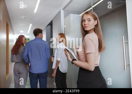 Photo sous angle d'une belle jeune femme d'affaires qui marche à l'intérieur le couloir avec son équipe créative Banque D'Images