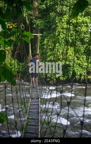 jeune homme marchant à travers le pont suspendu dans la jungle au-dessus d'un rivière Banque D'Images