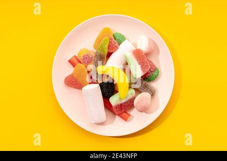Vue de dessus de délicieux bonbons multicolores sur une assiette rayée placé sur fond jaune Banque D'Images