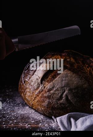 Rognez le boulanger anonyme avec un couteau en coupant du pain fraîchement préparé table en bois dans le bakehouse Banque D'Images