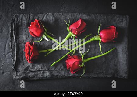 Composition de la vue de dessus des boutons roses rouges éclatants éparpillés sur une surface noire avec un chiffon Banque D'Images