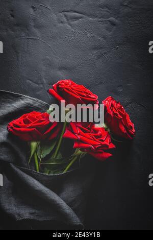 Composition de la vue de dessus des boutons roses rouges éclatants éparpillés sur une surface noire avec un chiffon Banque D'Images