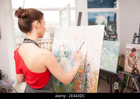 Vue arrière photo d'une jeune femme peignant une photo dans un studio d'art, espace de copie Banque D'Images