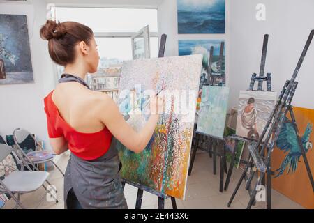 Vue arrière d'une artiste féminine non reconnaissable travaillant sur un tableau en classe d'art, espace de copie Banque D'Images