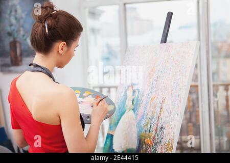 Vue arrière d'une jeune femme élégante peignant un photo à l'atelier d'art Banque D'Images