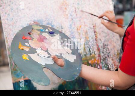 Gros plan d'une palette avec de la peinture à l'huile mélangée la main d'une artiste féminine Banque D'Images