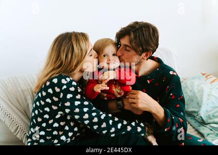 Parents amoureux en pyjama assis sur le lit et embrassant tendinement un tout petit tout en appréciant le week-end à la maison Banque D'Images