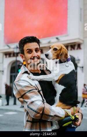 Contenu ethnique homme propriétaire avec mignon beagle chien debout rue et regarder la caméra Banque D'Images