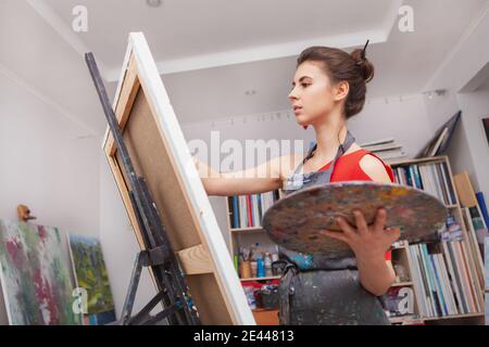 Photo sous angle d'une belle femme en train de peindre à son atelier. Dessin de peintre féminin dans un studio d'art Banque D'Images