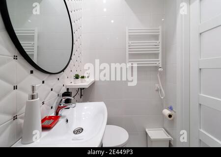 Une partie d'une petite salle de bains moderne dans un studio récemment meublé dans une maison ancienne. Murs carrelés de céramique, radiateur de serviette sur mur blanc, évier, mirr Banque D'Images