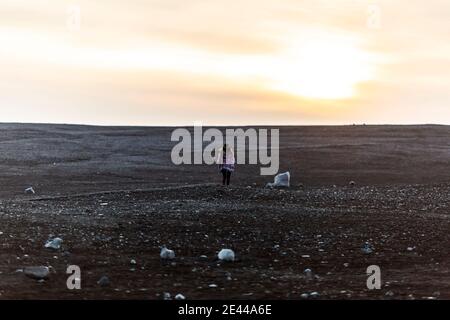 Vue arrière de la femme touristique anonyme debout dans un champ sec En hiver, en Islande et en admirant le coucher du soleil sur le ciel Banque D'Images