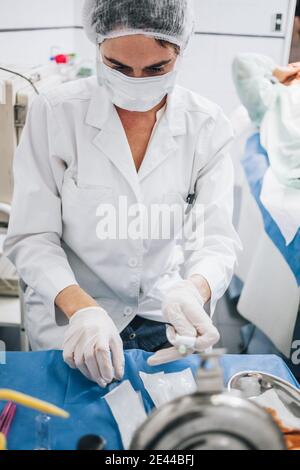 Photo verticale d'un médecin avec masque uniforme et protecteur et des gants assis devant une table avec des instruments pour fonctionner en cas de besoin Banque D'Images