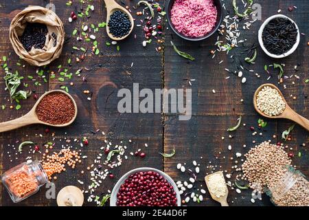 Vue de dessus des cuillères en bois remplies de différents grains composés en cercle sur une surface en bois rustique Banque D'Images