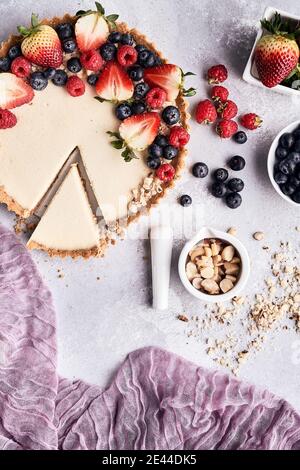 Du dessus de la tarte au cheesecake douce garnie d'un assortiment frais baies disposées sur la table avec des noix dans un bol Banque D'Images