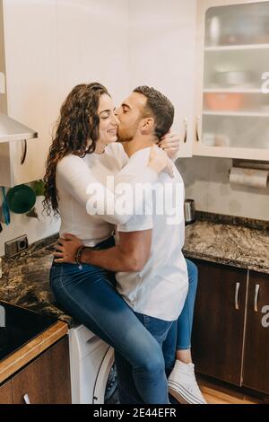 Vue latérale du contenu jeune couple debout dans la cuisine moderne à la maison et en vous embrassant tout en souriant et en regardant chacun autre Banque D'Images