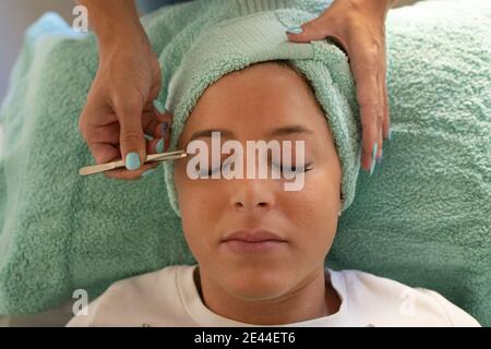 Grand angle de récolte une esthéticienne féminine non reconnaissable se défait procédure des sourcils du jeune client allongé sur le canapé pendant la procédure de beauté Banque D'Images