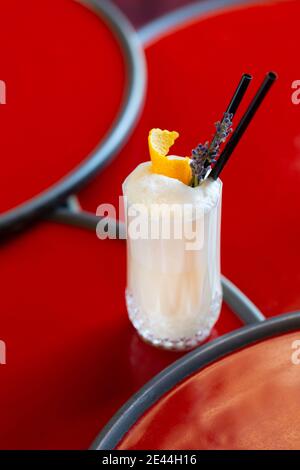 Verre de cocktail crémeux frais garni de zeste d'orange et fleur de lavande sur une table en bois sur fond rouge Banque D'Images
