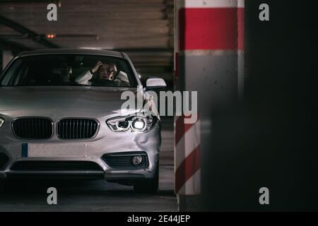 Une jeune femme choquée criait et touchait la tête après avoir frappé colonne en béton avec voiture dans le parking Banque D'Images
