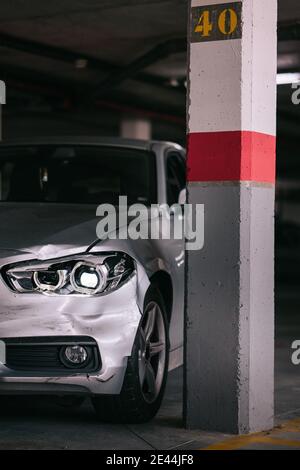 Voiture argentée moderne avec pare-chocs endommagé garée près d'une colonne de béton après un accident dans un garage Banque D'Images