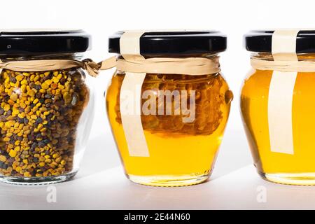 Pots en verre avec du miel frais et du pollen d'abeille placés dans ligne sur la table Banque D'Images