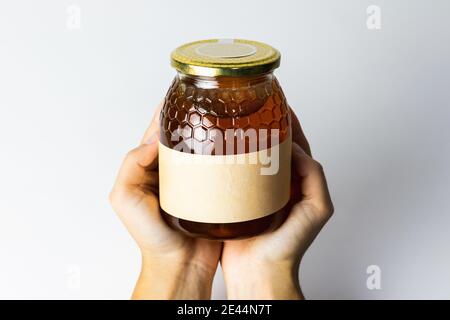 Crop-personne méconnaissable avec miel liquide naturel dans un pot en verre sur fond blanc Banque D'Images