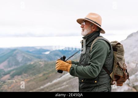 Homme voyageur senior en vêtements d'extérieur debout avec des jumelles dans les hautes terres Terrain et paysage pittoresque pendant les vacances d'hiver à Caceres Banque D'Images