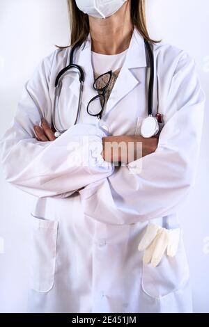 Femelle non reconnaissable, taillée en uniforme blanc et portant un stéthoscope masque médical de protection debout avec les bras croisés Banque D'Images