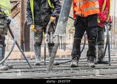 Un groupe de travailleurs de la construction pendant les travaux de moulage du béton, utilisant le vibrateur de béton pour compacter le béton de consistance raide. Banque D'Images