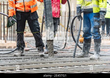 Un groupe de travailleurs de la construction pendant les travaux de moulage du béton, utilisant le vibrateur de béton pour compacter le béton de consistance raide. Banque D'Images