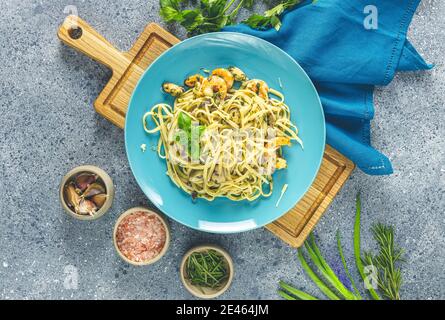 Pâtes linguine aux champignons, crevettes et moules de fruits de mer, fromage et herbes, en plaque de céramique bleue sur une surface gris clair. Banque D'Images