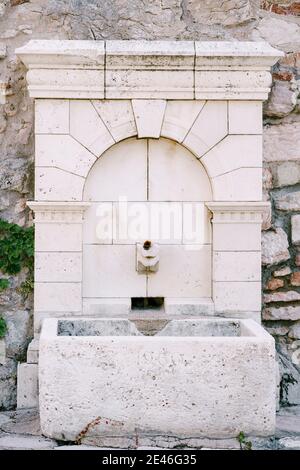 Une fontaine à boire carrelée avec un bol en pierre dans un mur pavé. Banque D'Images