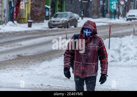 Montréal, CA - 21 janvier 2021: Homme avec masque facial drapeau du québec pour la protection contre la COVID-19 en descendant la rue pendant la tempête de neige Banque D'Images