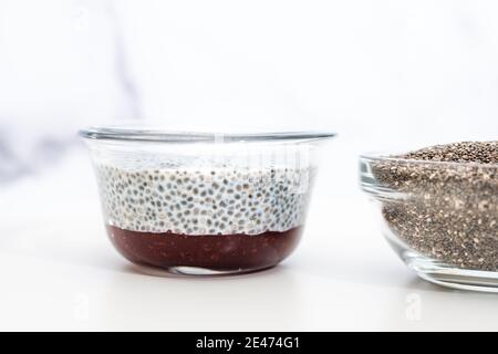 Pudding aux graines de Chia avec confiture de framboises dans un bol en verre gros plan sur fond blanc Banque D'Images