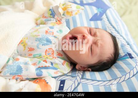 Vue du dessus de l'adorable petit bébé asiatique bâillonne avant de dormir sur le lit Banque D'Images