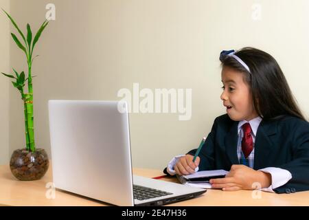 Belle fille colombienne portant un uniforme d'école faisant ses devoirs son ordinateur portable Banque D'Images