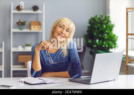 Une femme d'âge moyen positive qui travaille au bureau regarde caméra pendant la journée de travail Banque D'Images