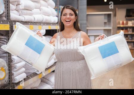 Une femme au foyer mûre et excitée rit, achetant de nouveaux oreillers orthopédiques en vente dans un grand magasin Banque D'Images