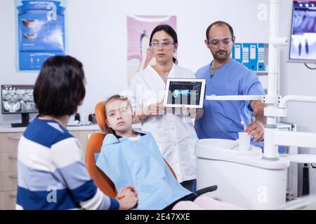 Dentiste pédiatrique avec radiographie numérique de la petite fille de dent sur un Tablet pc. Stomatologue expliquant le diagnostic des dents à la mère de l'enfant dans la clinique de santé tenant des rayons X. Banque D'Images