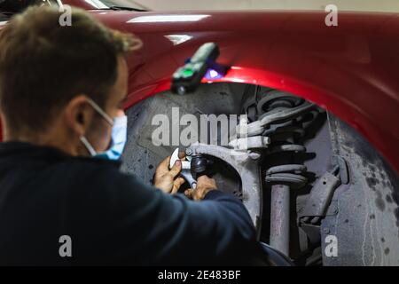 mécanicien répare la suspension de voiture. Concentrez-vous sur les mains. COVID 19 Banque D'Images