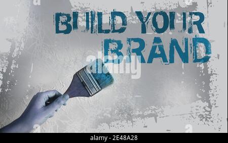 Construisez vos mots de marque sur le mur gris avec le pinceau dans la main. Concept de marketing d'entreprise motivationnel. Banque D'Images