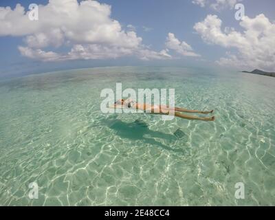 Jeune belle femme couché et flottant sur le dos dans l'eau turquoise de mer sur la plage tropicale paradisiaque à Bora Bora, Polynésie française. Vacances et Banque D'Images