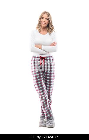 Jolie jeune femme en pyjama avec des mains croisées qui se tortillent à l'appareil photo et sourire. Portrait intégral sur fond blanc. Banque D'Images