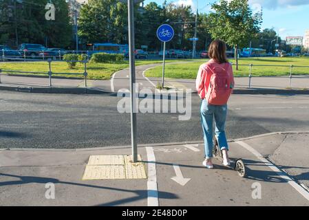 Fille sur scooter été dans la ville. Se tient avec son dos, à la croisée des chemins, en attendant que la voiture passe. Copie de texte dans l'espace libre. Conformité aux règles de sécurité routière Banque D'Images